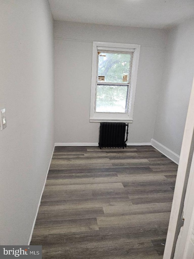 spare room with radiator heating unit, baseboards, and wood finished floors