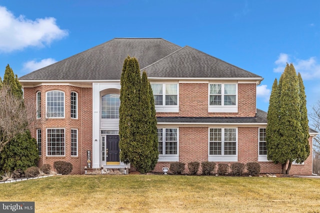 view of front of property featuring brick siding, roof with shingles, and a front yard