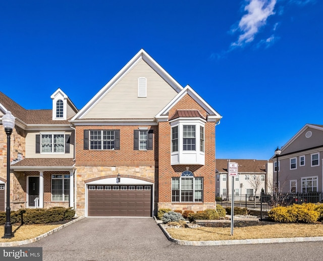 townhome / multi-family property with brick siding, an attached garage, fence, stone siding, and driveway