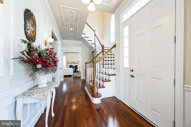 entrance foyer with a glass covered fireplace, dark wood-style flooring, visible vents, and stairway