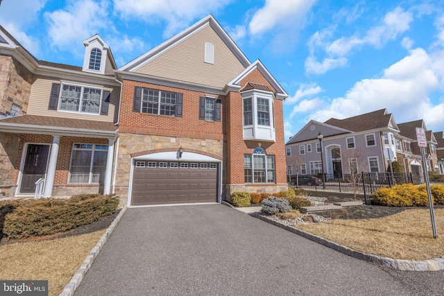 view of property featuring driveway, a garage, stone siding, fence, and brick siding