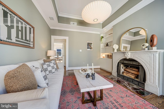 living room featuring baseboards, built in features, a tray ceiling, crown molding, and a fireplace