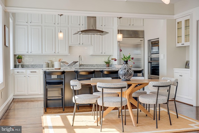 kitchen featuring light wood finished floors, a breakfast bar, island exhaust hood, pendant lighting, and built in fridge