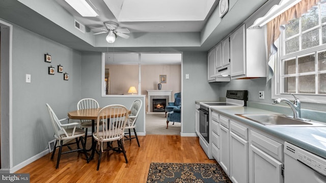 kitchen with electric stove, light countertops, a glass covered fireplace, a sink, and dishwasher