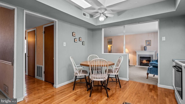 dining area featuring light wood-type flooring, a high end fireplace, visible vents, and a ceiling fan