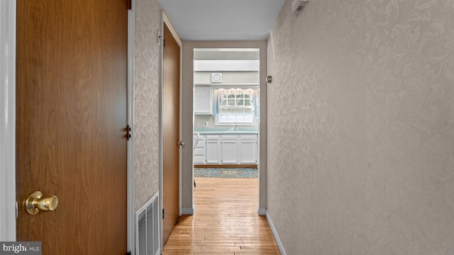 corridor featuring light wood-style floors, visible vents, a sink, and a textured wall