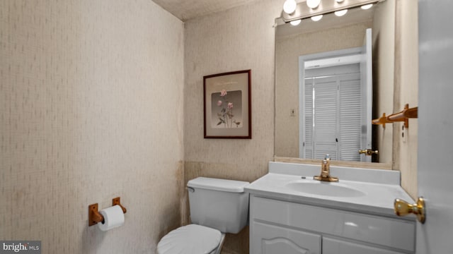 bathroom featuring vanity, toilet, and wallpapered walls