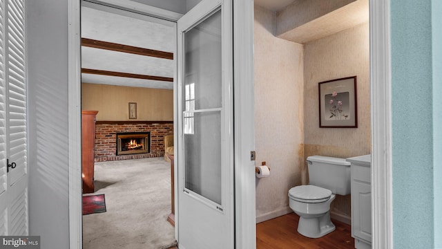 bathroom featuring toilet, a brick fireplace, and wood finished floors