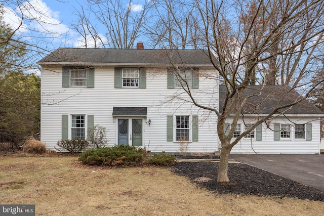 colonial inspired home featuring driveway, a shingled roof, a chimney, and a front yard