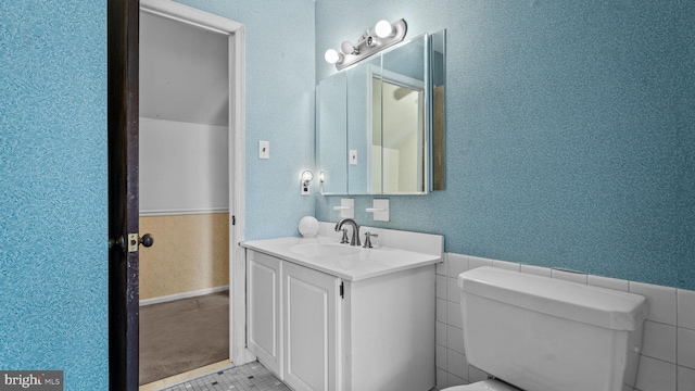 half bath with a wainscoted wall, tile walls, toilet, vanity, and tile patterned flooring