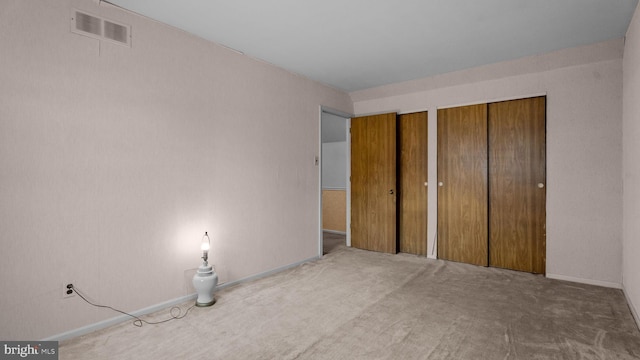 unfurnished bedroom featuring multiple closets, visible vents, and carpet floors