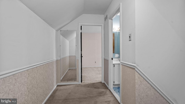 hallway featuring lofted ceiling, wainscoting, visible vents, and light colored carpet