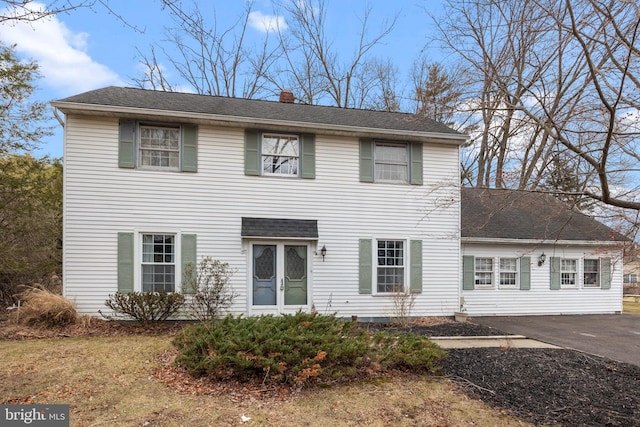 colonial inspired home with roof with shingles, driveway, and a chimney