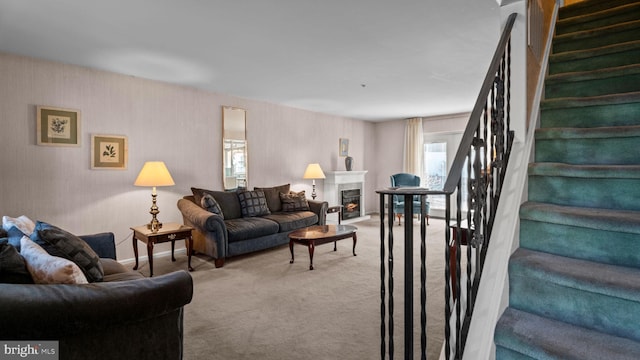 carpeted living area with a lit fireplace and stairs