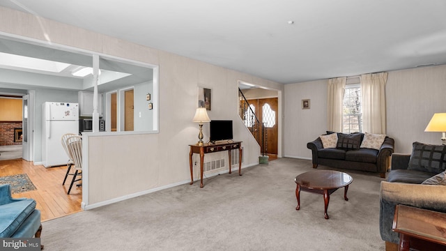 living room featuring a skylight, baseboards, stairway, and light colored carpet