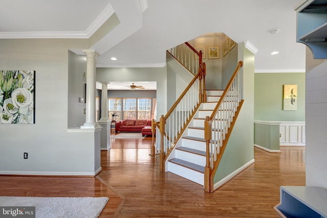 stairway with decorative columns, ornamental molding, ceiling fan, and wood finished floors