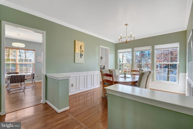 dining space with a chandelier, ornamental molding, a wainscoted wall, and wood finished floors