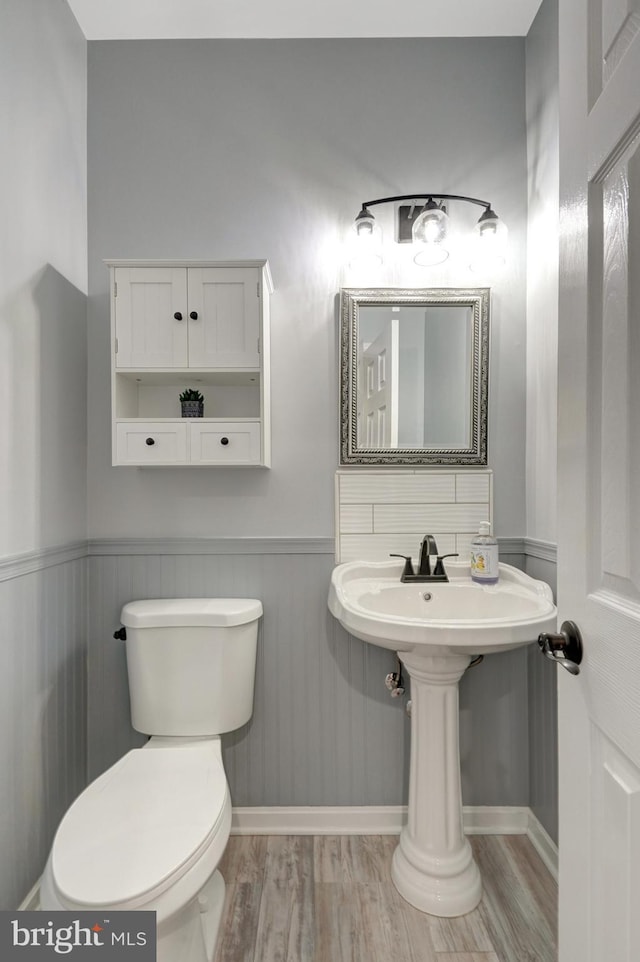 half bathroom with a wainscoted wall, toilet, and wood finished floors