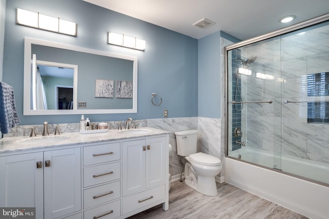 full bathroom featuring wood finished floors, combined bath / shower with glass door, a sink, and visible vents