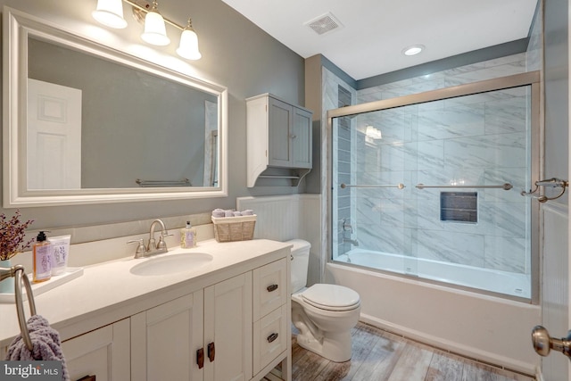 full bath with bath / shower combo with glass door, visible vents, toilet, vanity, and wood finished floors