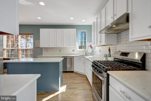 kitchen with under cabinet range hood, a healthy amount of sunlight, white cabinets, appliances with stainless steel finishes, and light stone countertops