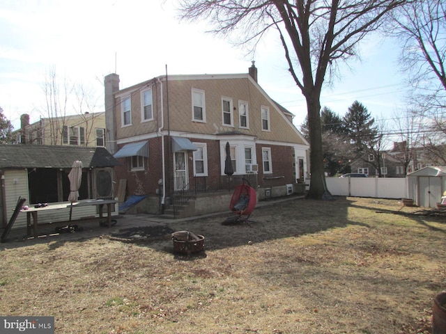 back of house featuring a fire pit, a storage unit, a chimney, and fence