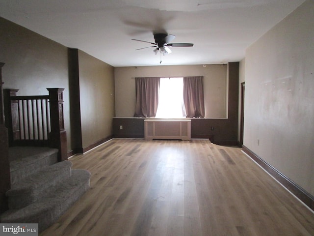 empty room featuring stairs, baseboards, wood finished floors, and radiator