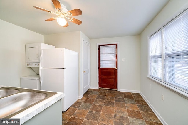 kitchen with baseboards, a ceiling fan, stacked washer / drying machine, freestanding refrigerator, and light countertops