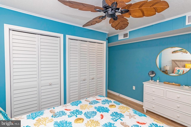 bedroom with ceiling fan, wood finished floors, visible vents, multiple closets, and ornamental molding