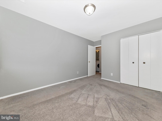 unfurnished bedroom featuring carpet floors, washer / dryer, a closet, and baseboards