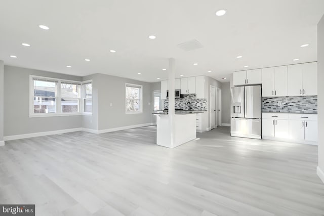 kitchen featuring stainless steel fridge, white cabinets, dark countertops, an island with sink, and open floor plan