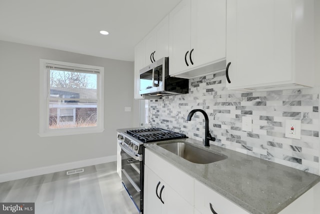 kitchen featuring stainless steel appliances, a sink, white cabinets, light stone countertops, and tasteful backsplash