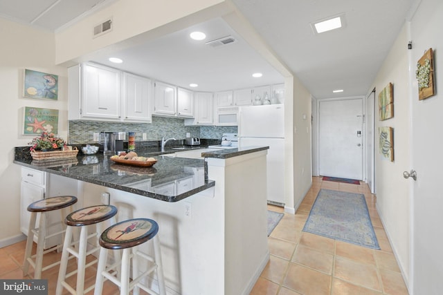 kitchen with white appliances, visible vents, decorative backsplash, dark stone counters, and a peninsula