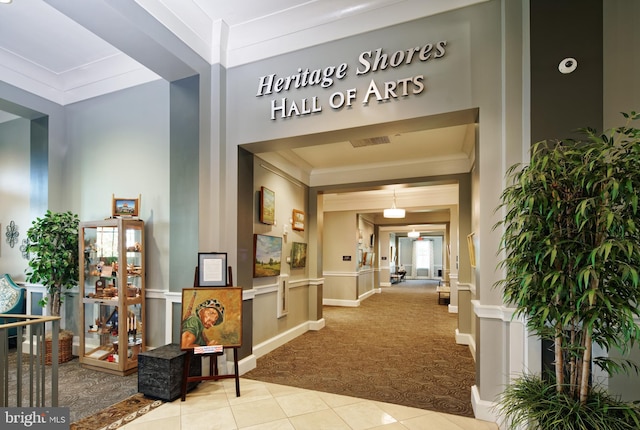 interior space featuring light tile patterned floors, a decorative wall, light colored carpet, and crown molding