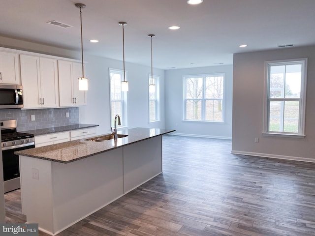 kitchen featuring a center island with sink, dark stone counters, stainless steel appliances, white cabinetry, and a sink