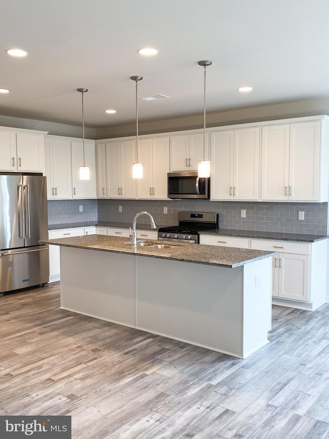 kitchen featuring appliances with stainless steel finishes, pendant lighting, white cabinetry, and an island with sink