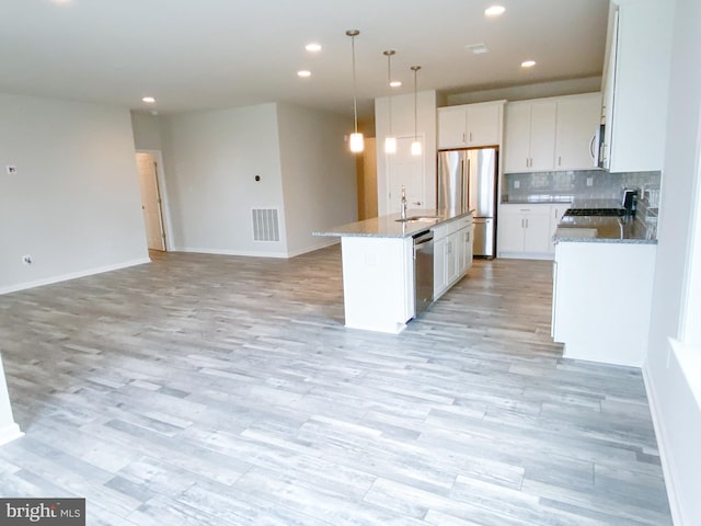 kitchen featuring visible vents, appliances with stainless steel finishes, white cabinetry, a sink, and an island with sink