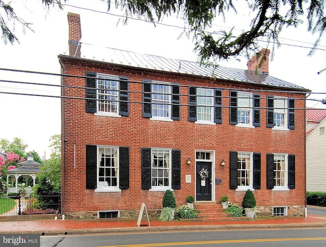 colonial inspired home featuring entry steps, brick siding, and a chimney