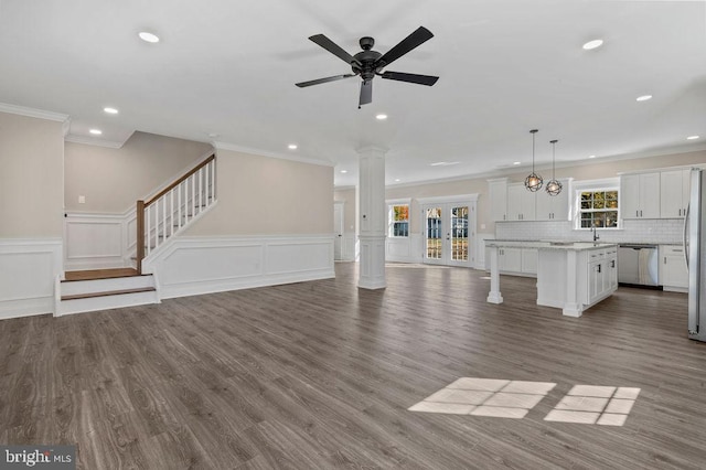 unfurnished living room featuring ornate columns, stairs, ornamental molding, and wood finished floors