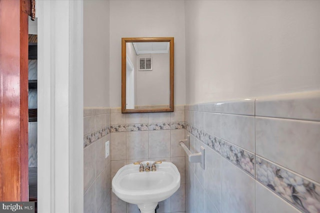 bathroom with a wainscoted wall, visible vents, a sink, and tile walls