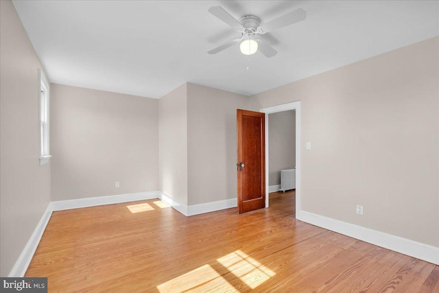 empty room with baseboards, radiator heating unit, and light wood-style floors