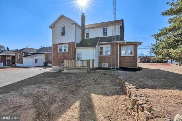 rear view of property featuring a chimney and brick siding