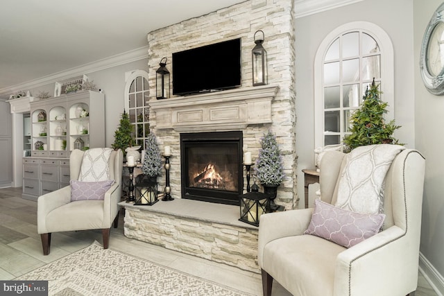 sitting room with ornamental molding, a stone fireplace, and wood finished floors