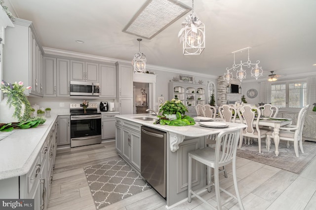 kitchen with pendant lighting, a center island with sink, stainless steel appliances, gray cabinets, and a sink