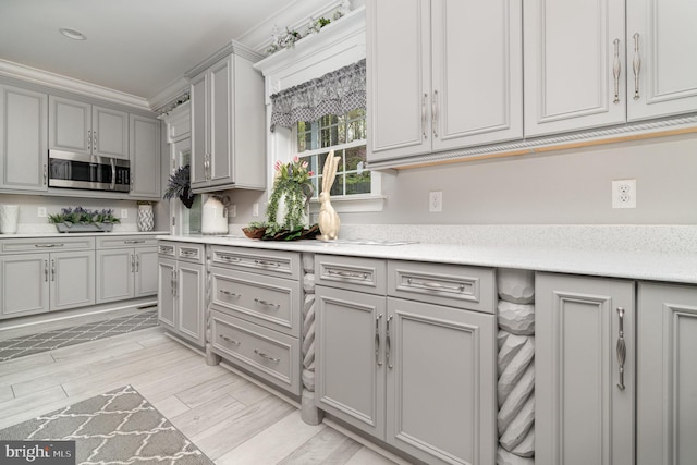 kitchen featuring crown molding, gray cabinets, light countertops, stainless steel microwave, and light wood-type flooring