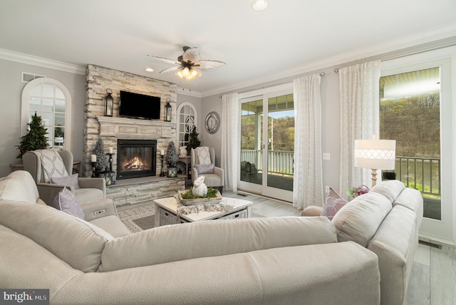 living room with ornamental molding, light wood-type flooring, visible vents, and a stone fireplace