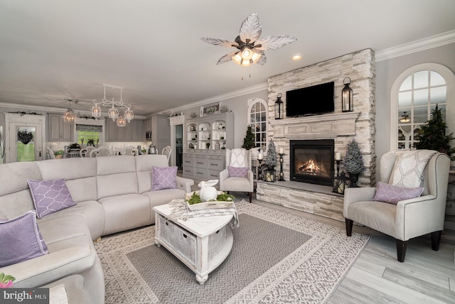 living room featuring light wood-type flooring, a ceiling fan, crown molding, and a stone fireplace