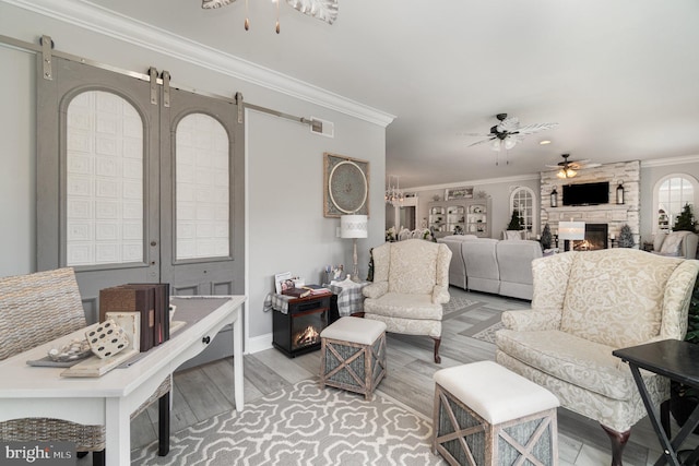 living area with a barn door, visible vents, ceiling fan, crown molding, and a fireplace