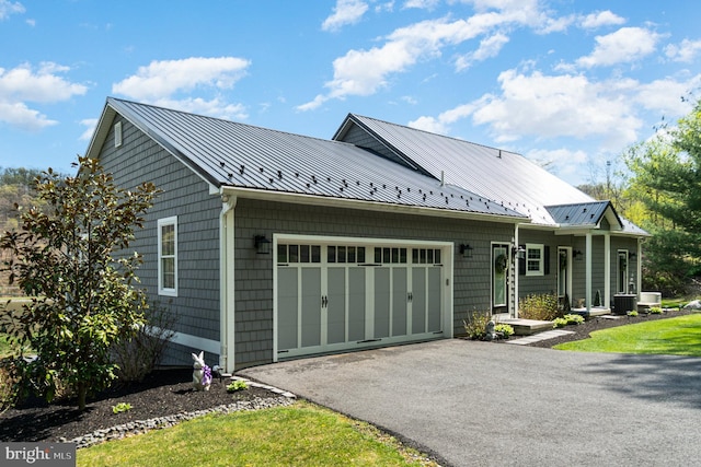 view of front facade with metal roof, an attached garage, cooling unit, driveway, and a standing seam roof