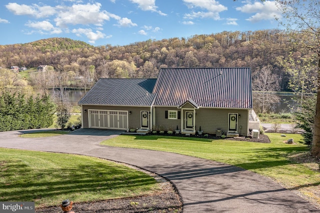 view of front facade featuring entry steps, metal roof, a garage, driveway, and a front lawn